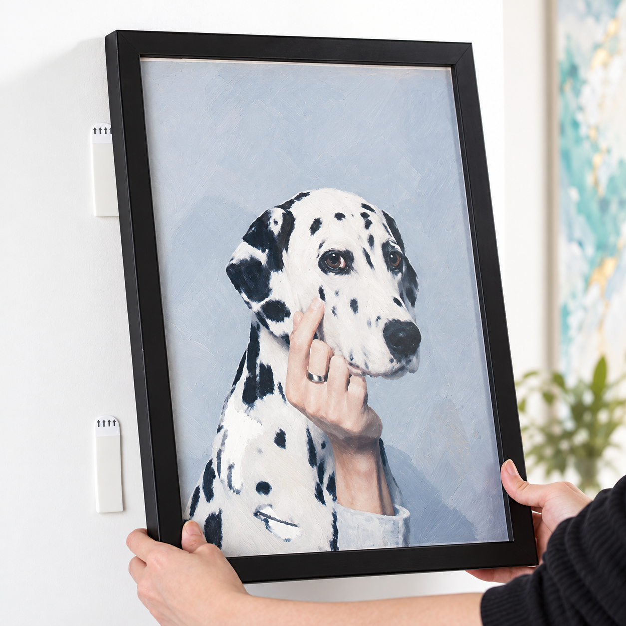 Zwei Hände halten einen schwarzen Bilderrahmen neben weißen Klebestreifen an einer hellen Wand.